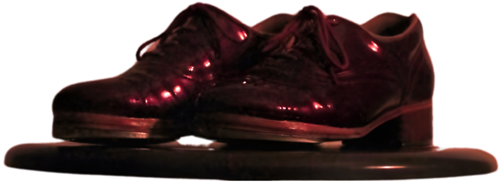 Close-up of a shiny, dark-colored leather dress shoe with laces, resting on a reflective surface.