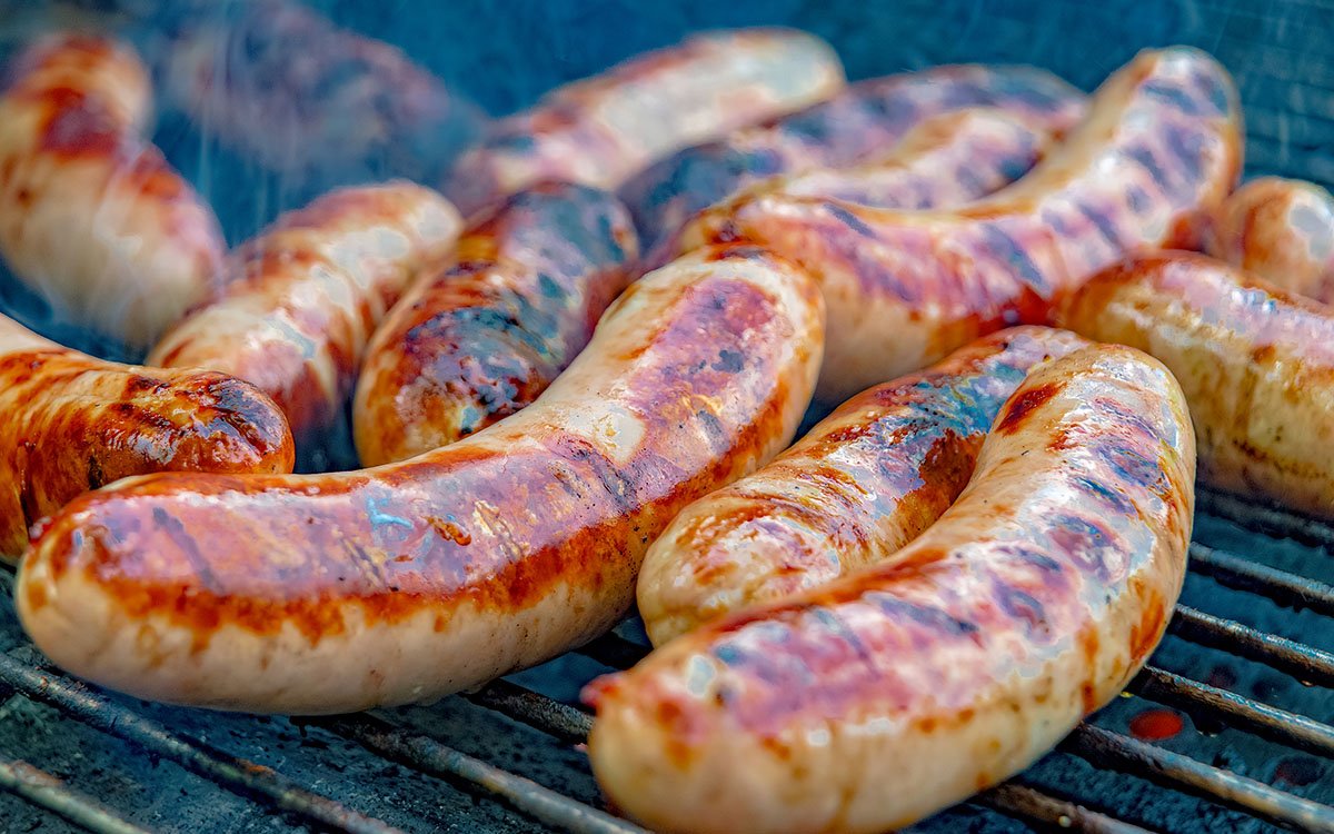 Several sausages cooking on a grill with grill marks.