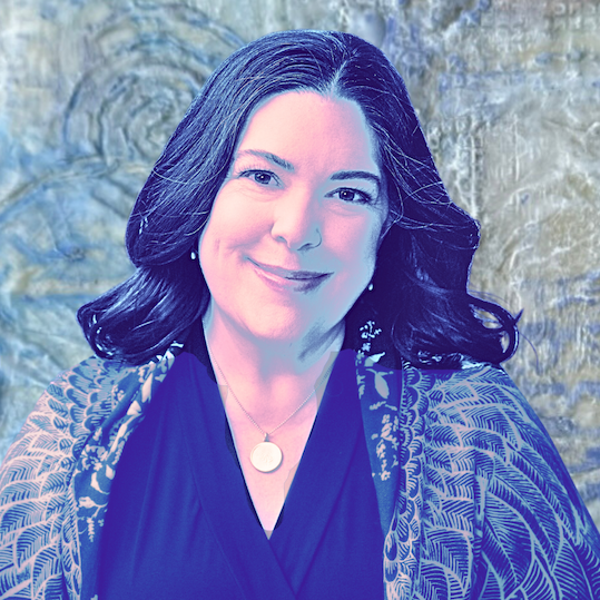 A woman with dark hair smiling, wearing a dark top and a patterned shawl, standing in front of a textured stone wall.