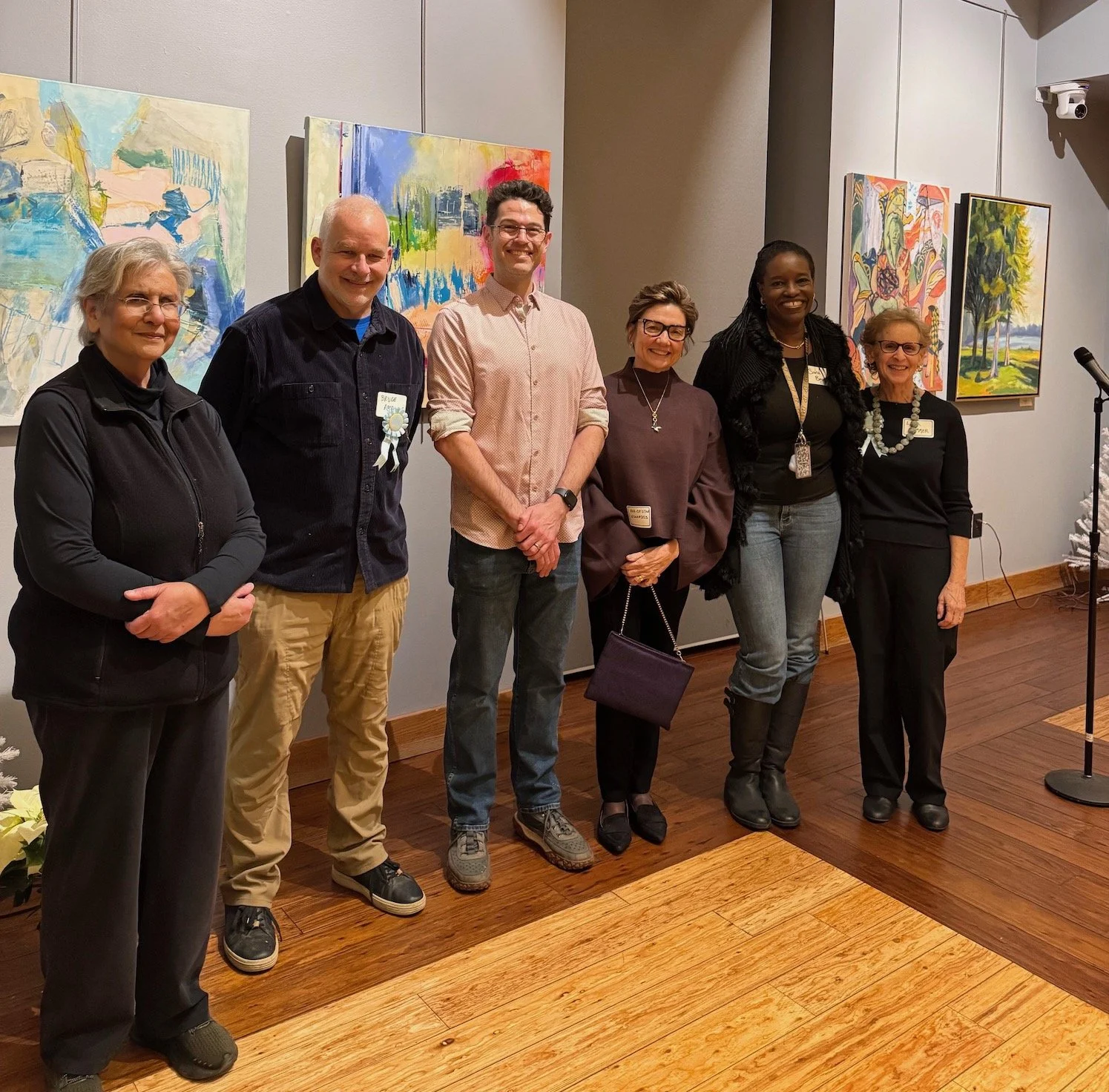 Six people standing in front of colorful abstract paintings in an art gallery, smiling for the photo.