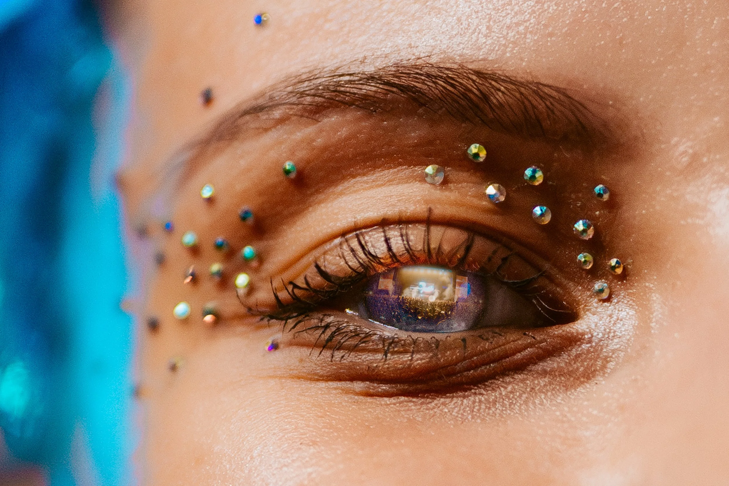Close-up of a person's eye with makeup, rhinestones around the eye, and a reflection in the iris.
