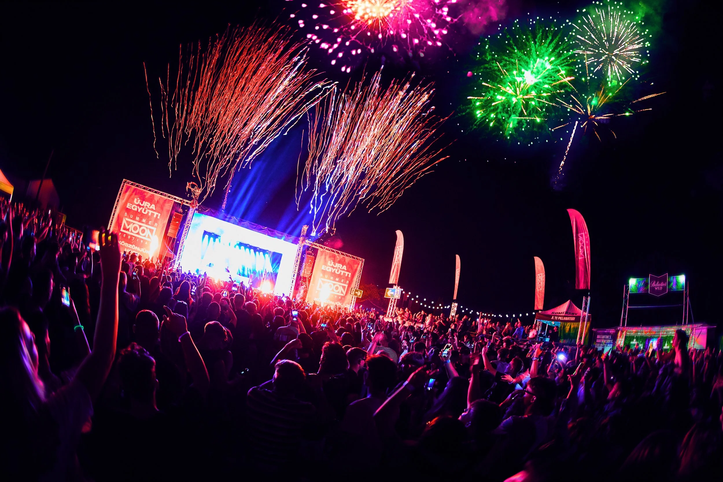 Crowd watching fireworks and a concert stage at night during a celebration.