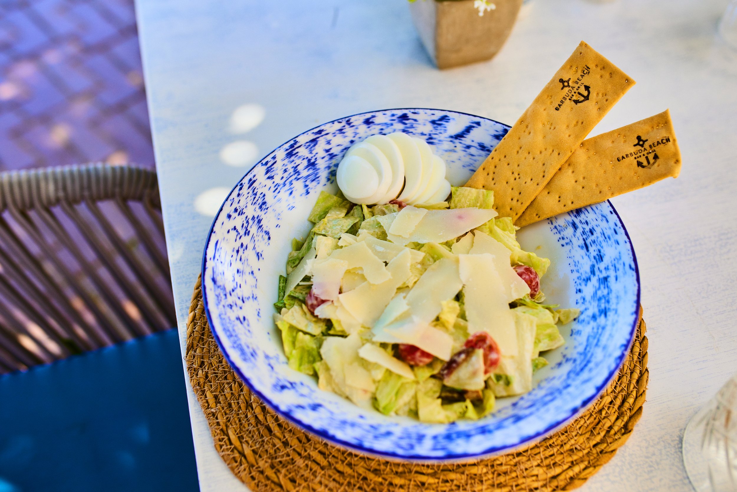 Caesar salad in a blue and white bowl with two crispy breadsticks and a dollop of mayonnaise.