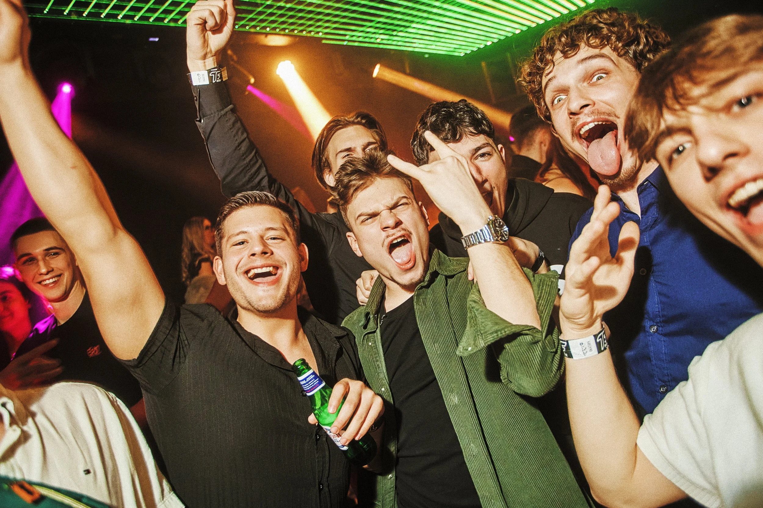 Group of young people celebrating and having fun at a party or club with colorful lights and energetic expressions.