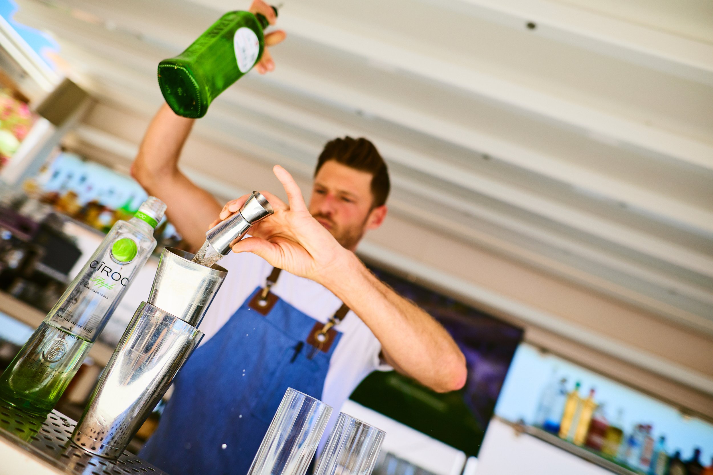 Bartender pouring CÎROC vodka into a shaker at a bar with bottles on display in the background.
