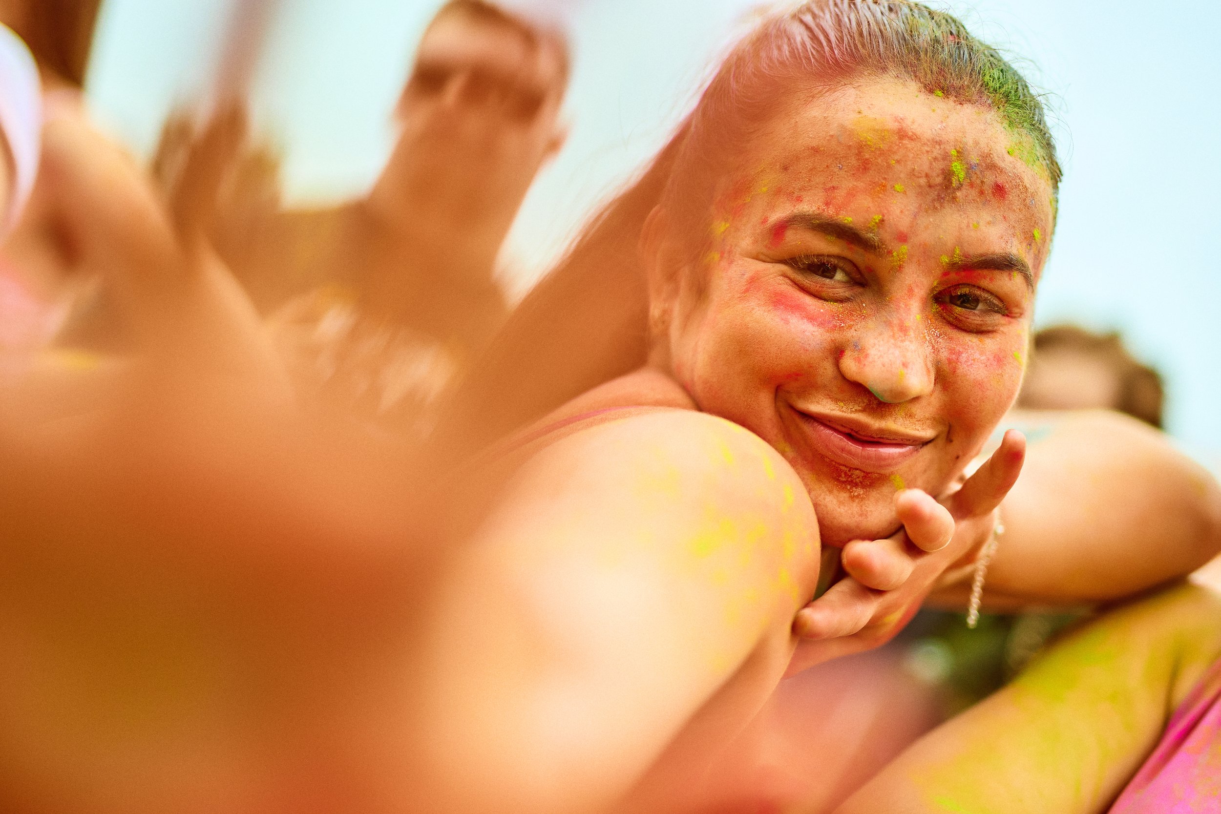 A young woman participating in a colorful festival or celebration, covered in vibrant powders and smiling.