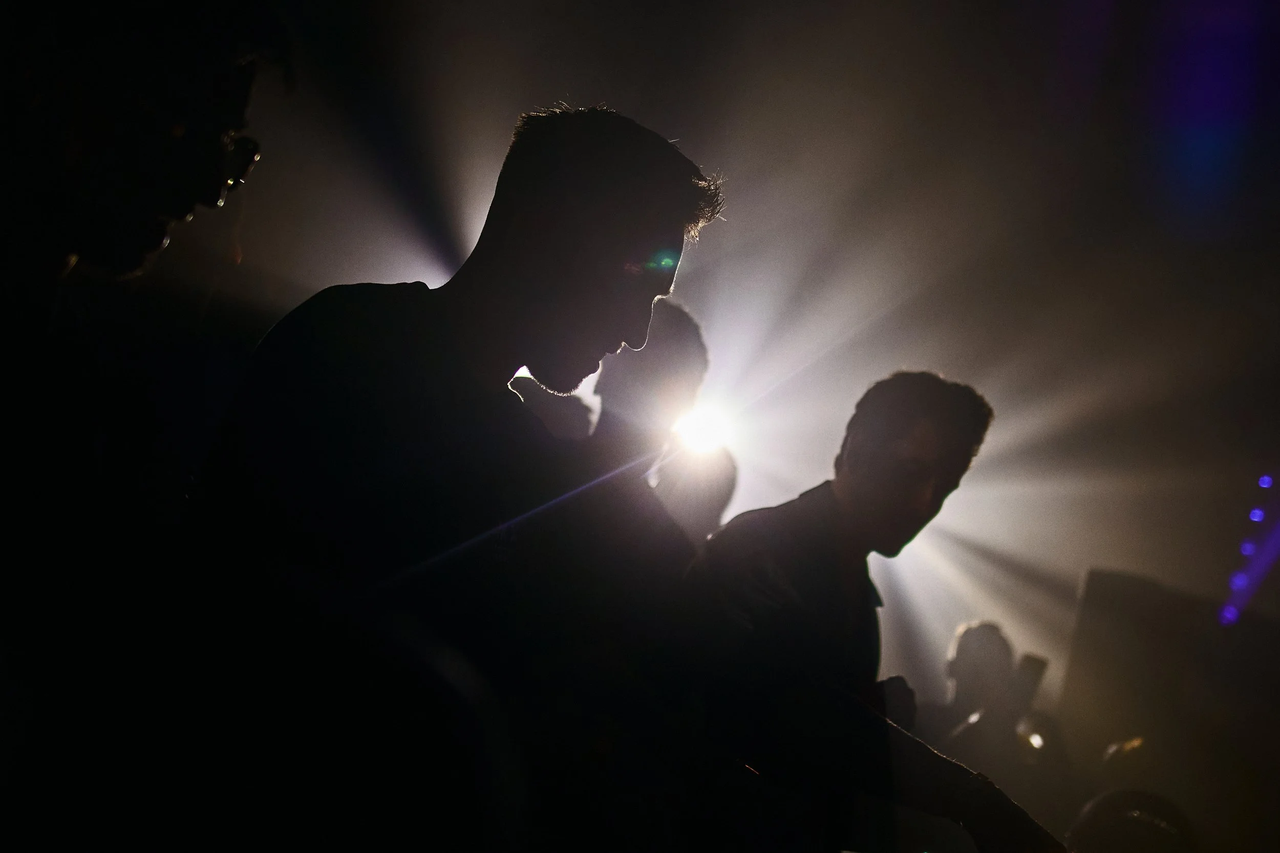Silhouettes of DJ performers at a nightclub with backlighting and light rays.