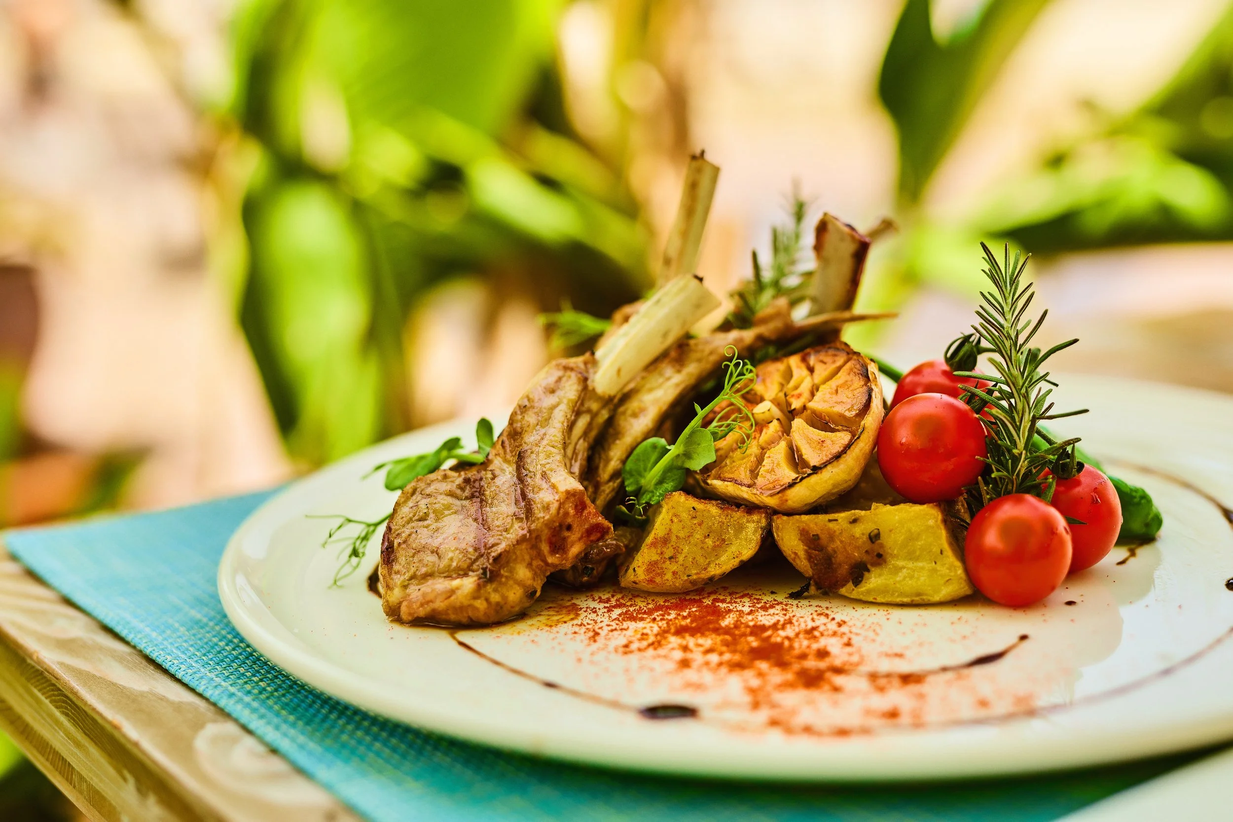A plated gourmet dish with lamb chops, roasted vegetables, cherry tomatoes, and fresh herbs, garnished with spices.