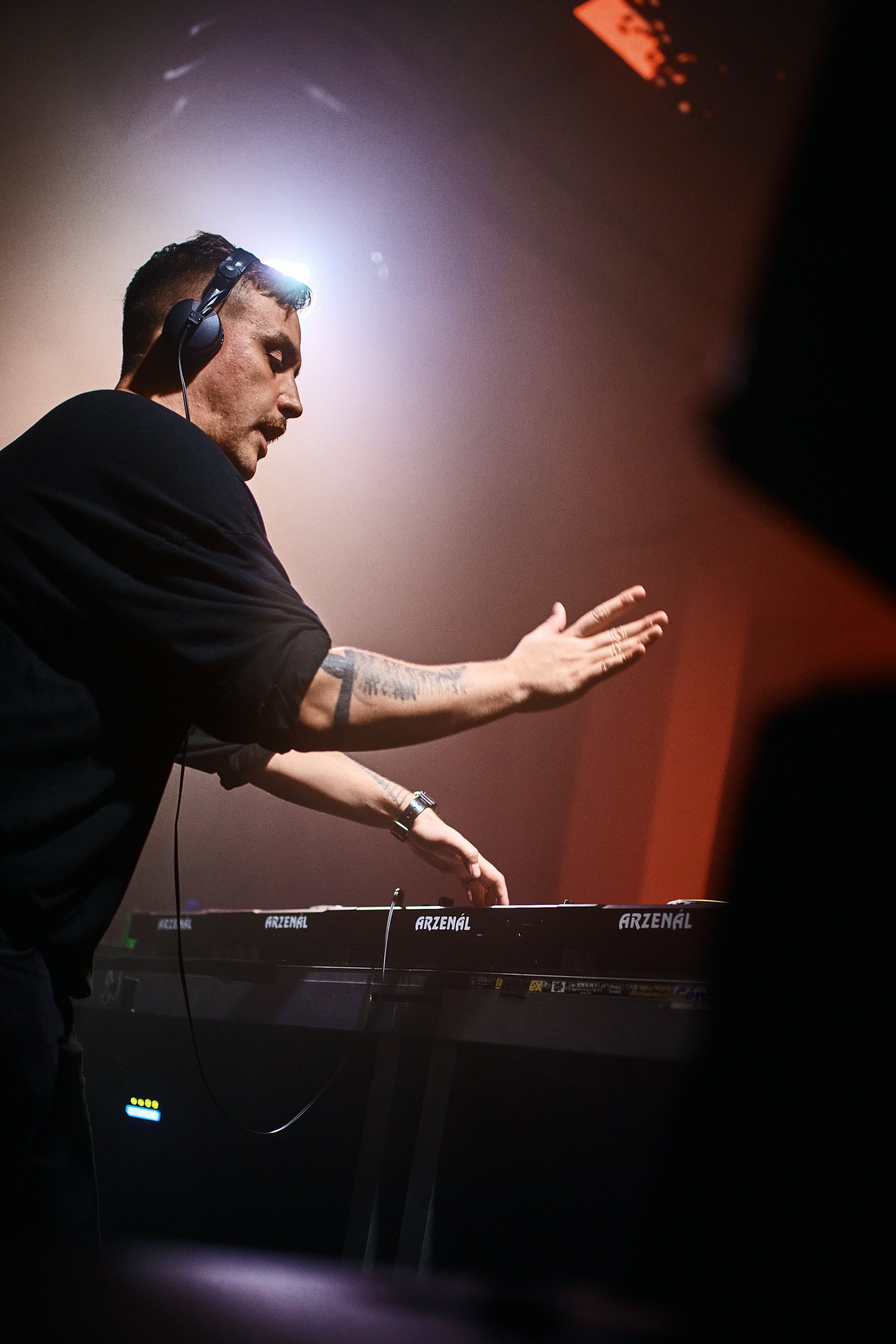 A DJ wearing headphones and a black shirt, mixing music on a digital keyboard during a live performance.