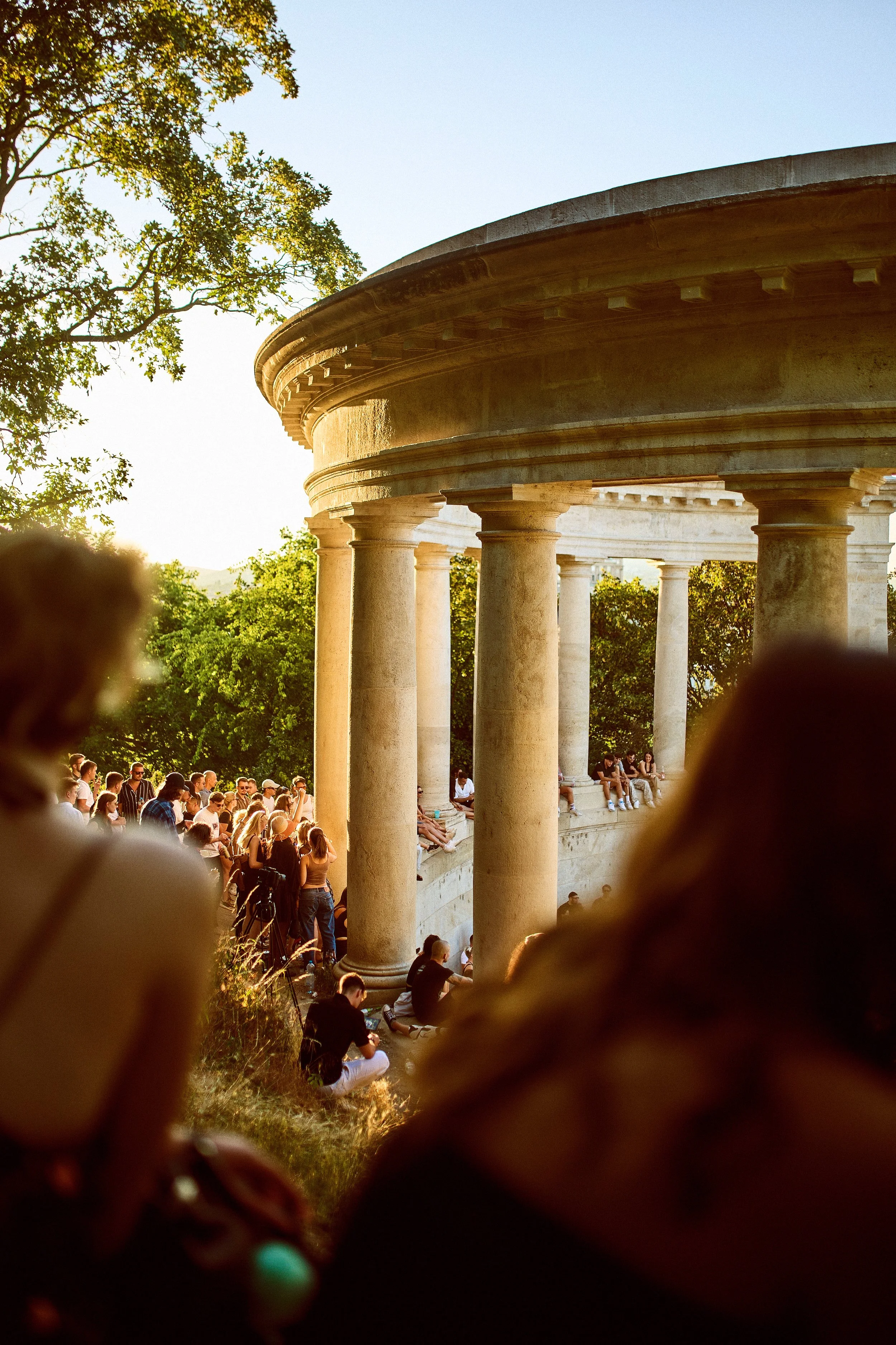 Crowd of people gathered around and sitting near the Lincoln Memorial in Washington, D.C., during sunset.