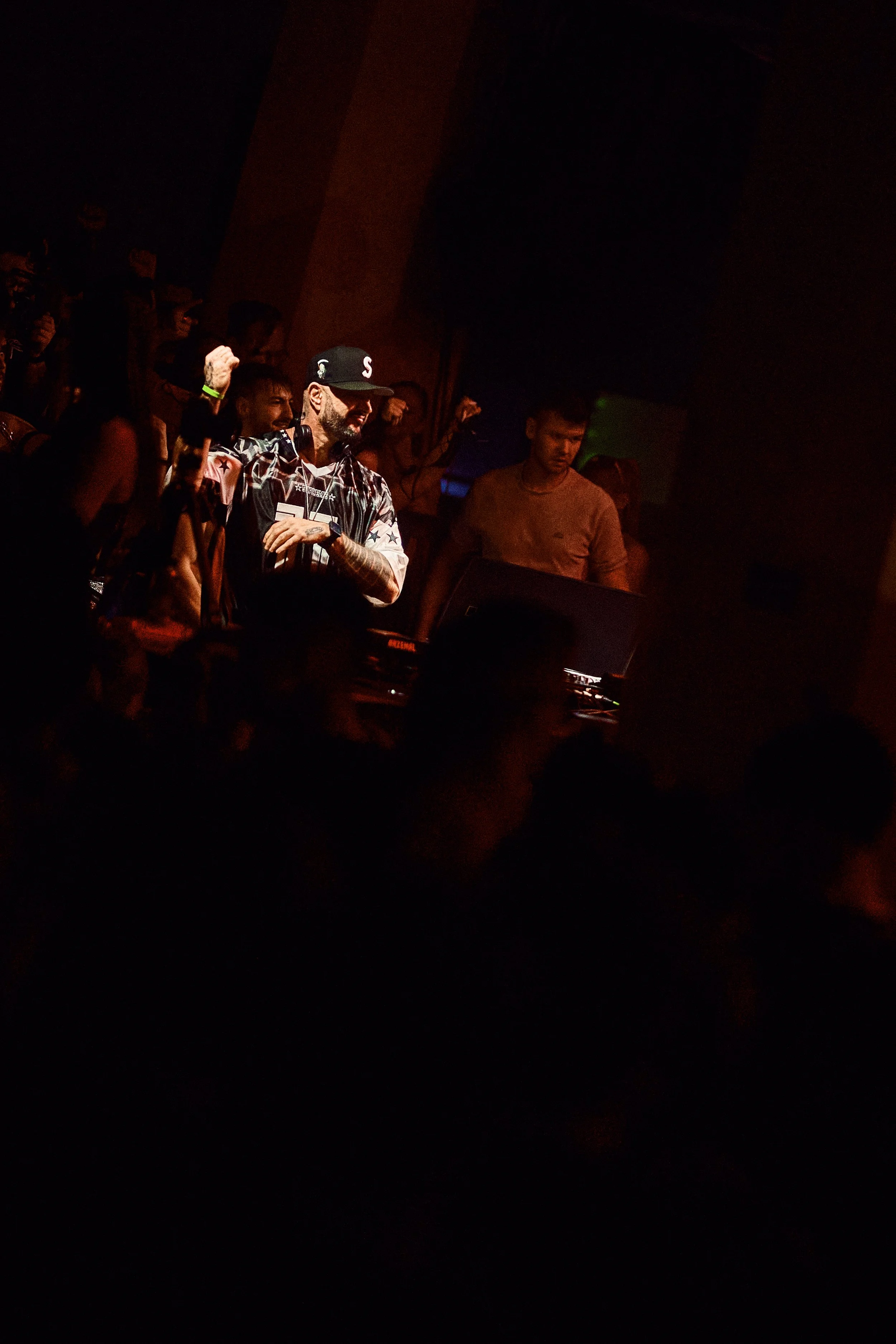 A DJ performs at a crowded nightclub with partygoers dancing and raising their hands
