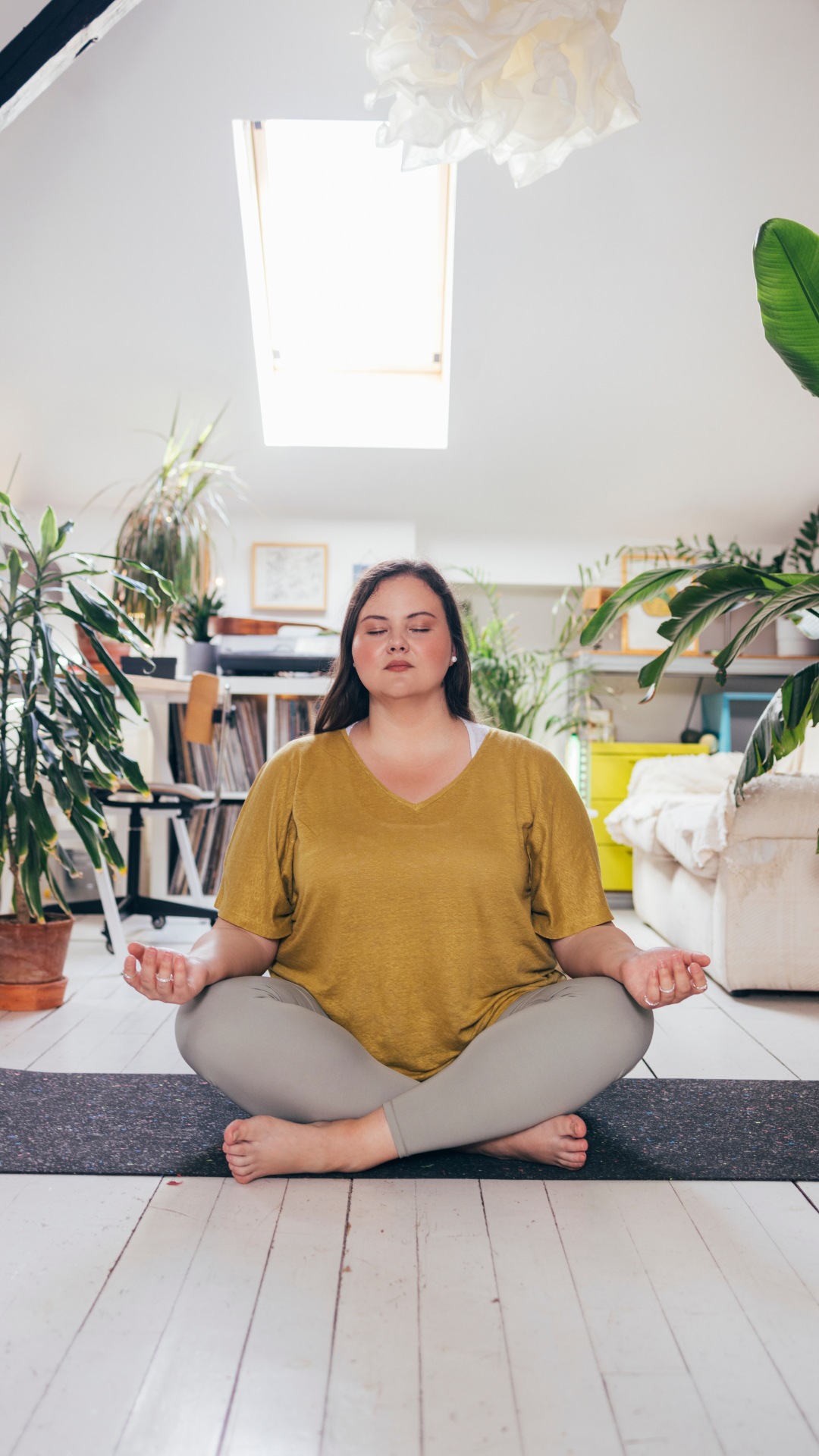 ADHD Woman sitting cross-legged on a yoga mat at home with eyes closed, practicing a simple grounding meditation in a calm living space
