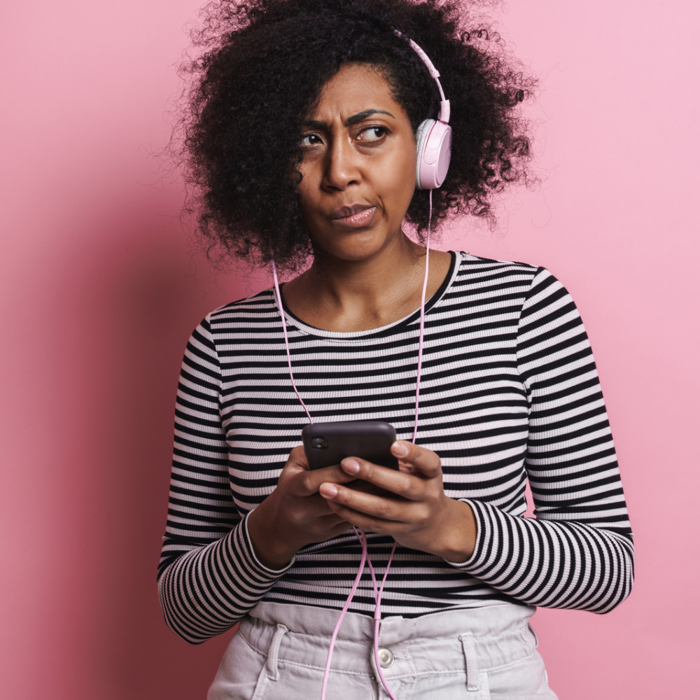 A woman wearing headphones looks puzzled while listening to a meditation on her phone.