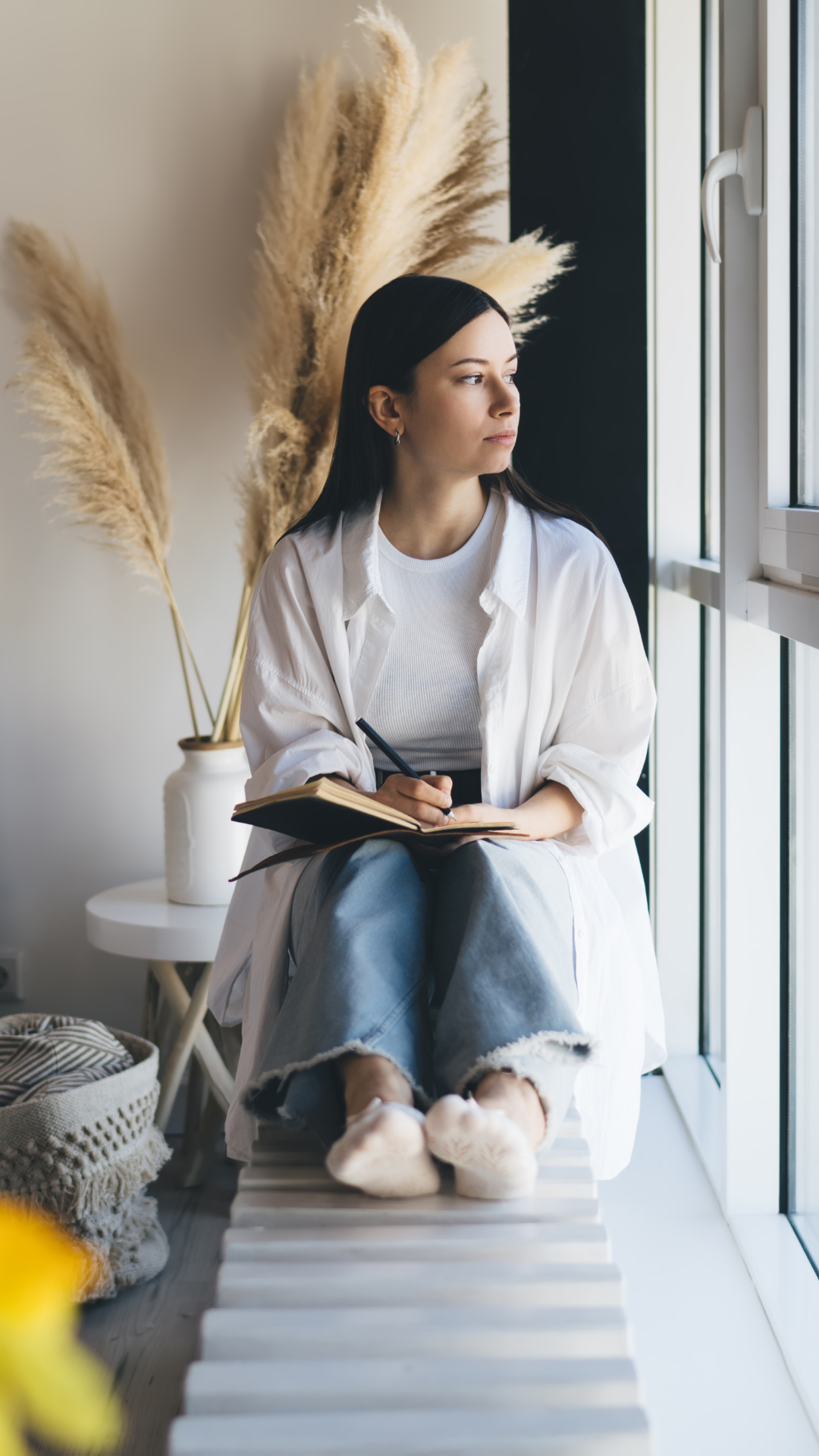 A woman writing in a notebook by a window as part of a self-study practice.