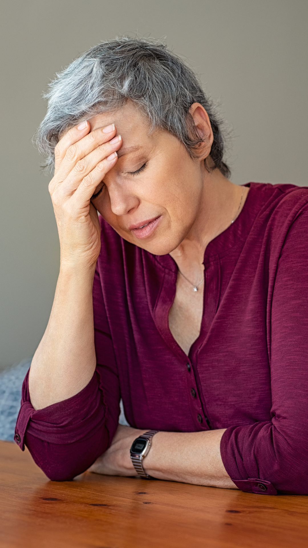 Woman sitting at a table with hand on her forehead showing overwhelm and mental fatigue