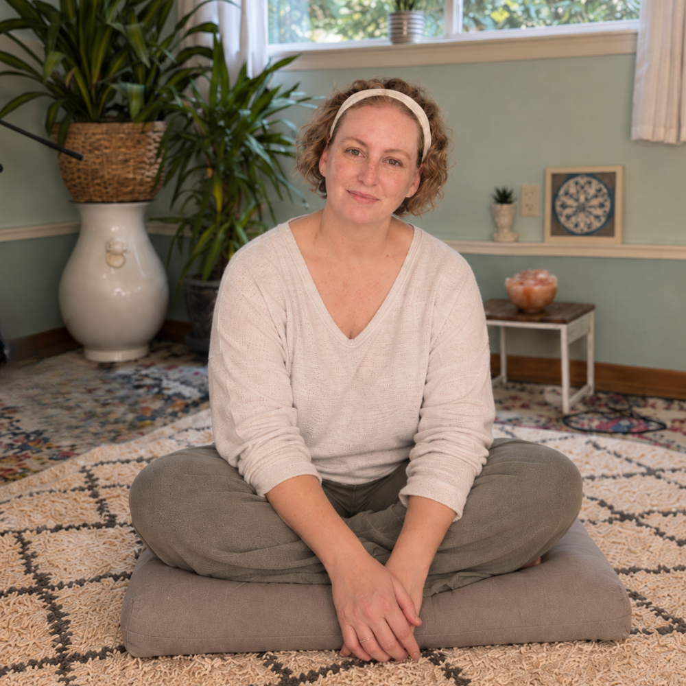 Tonya Rothe seated cross-legged on a cushion in her home yoga space.