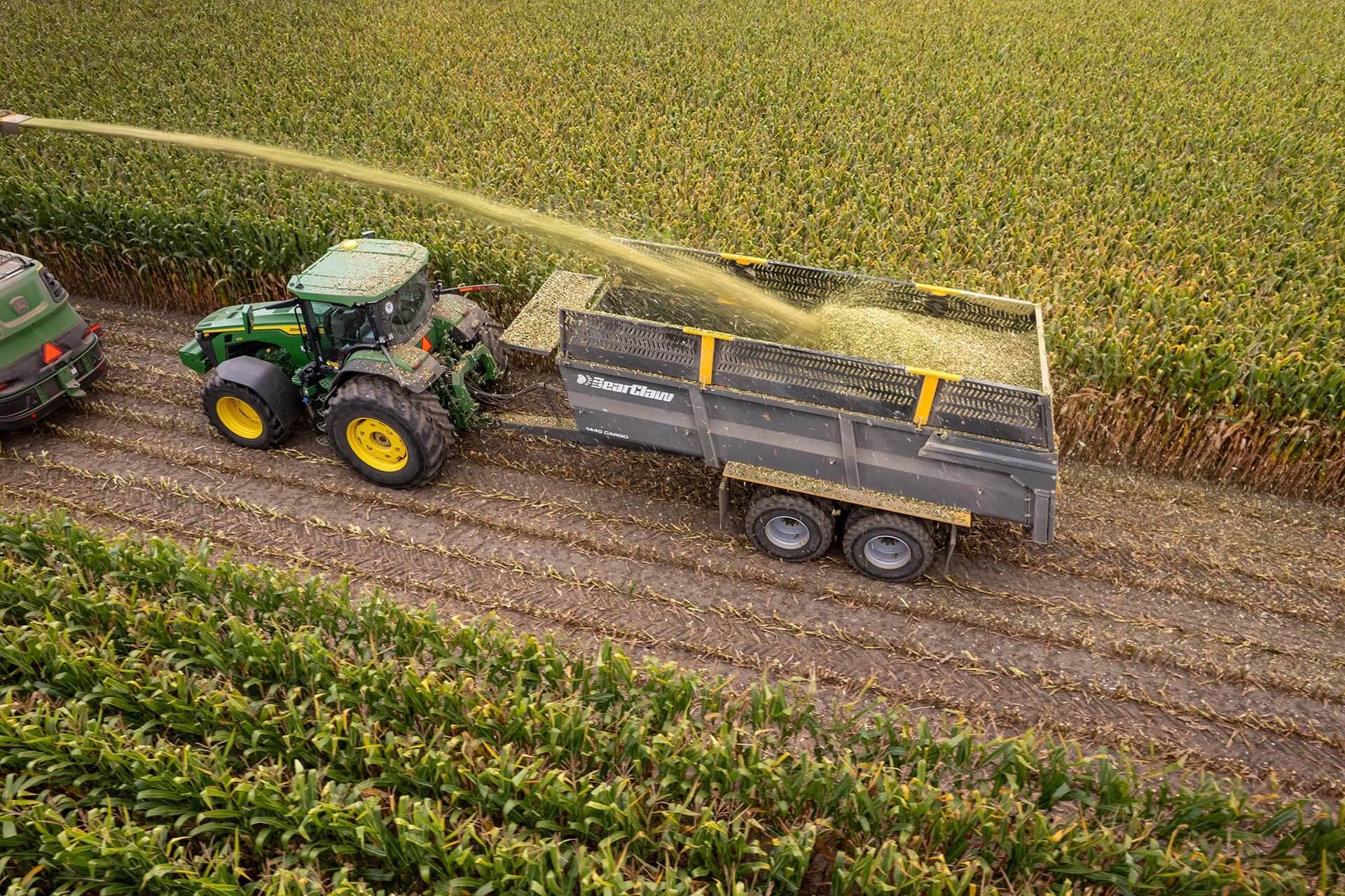 A tractor watering a large field of crops, with a trailer attached and another vehicle nearby.