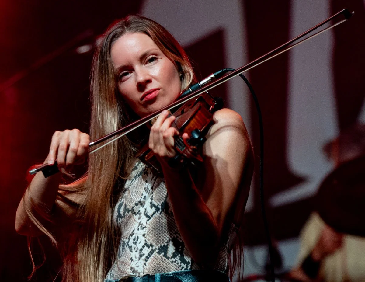 A woman with long hair playing the violin, looking thoughtfully