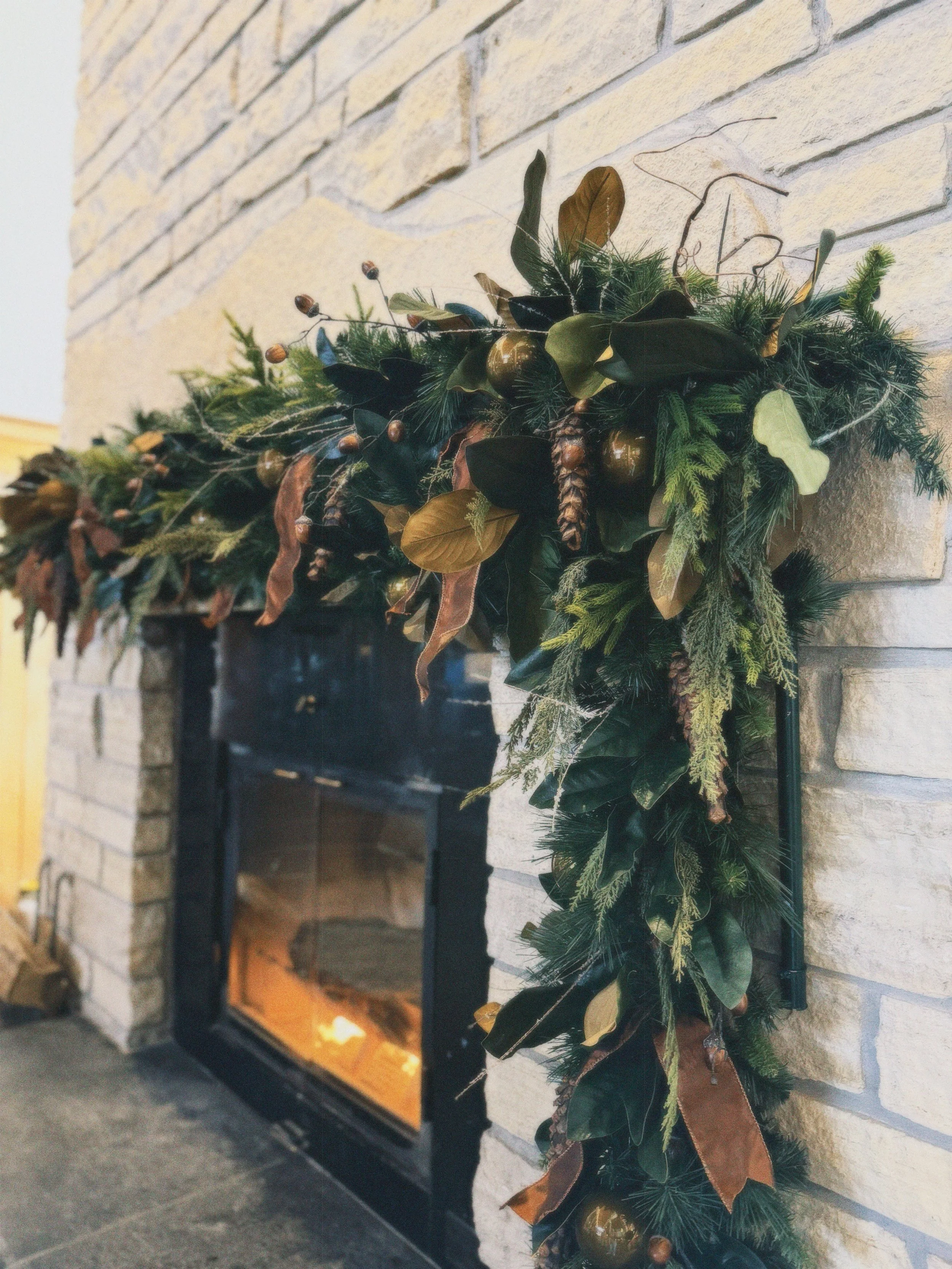 Decorative Christmas garland hanging on a brick fireplace with a fire burning inside.