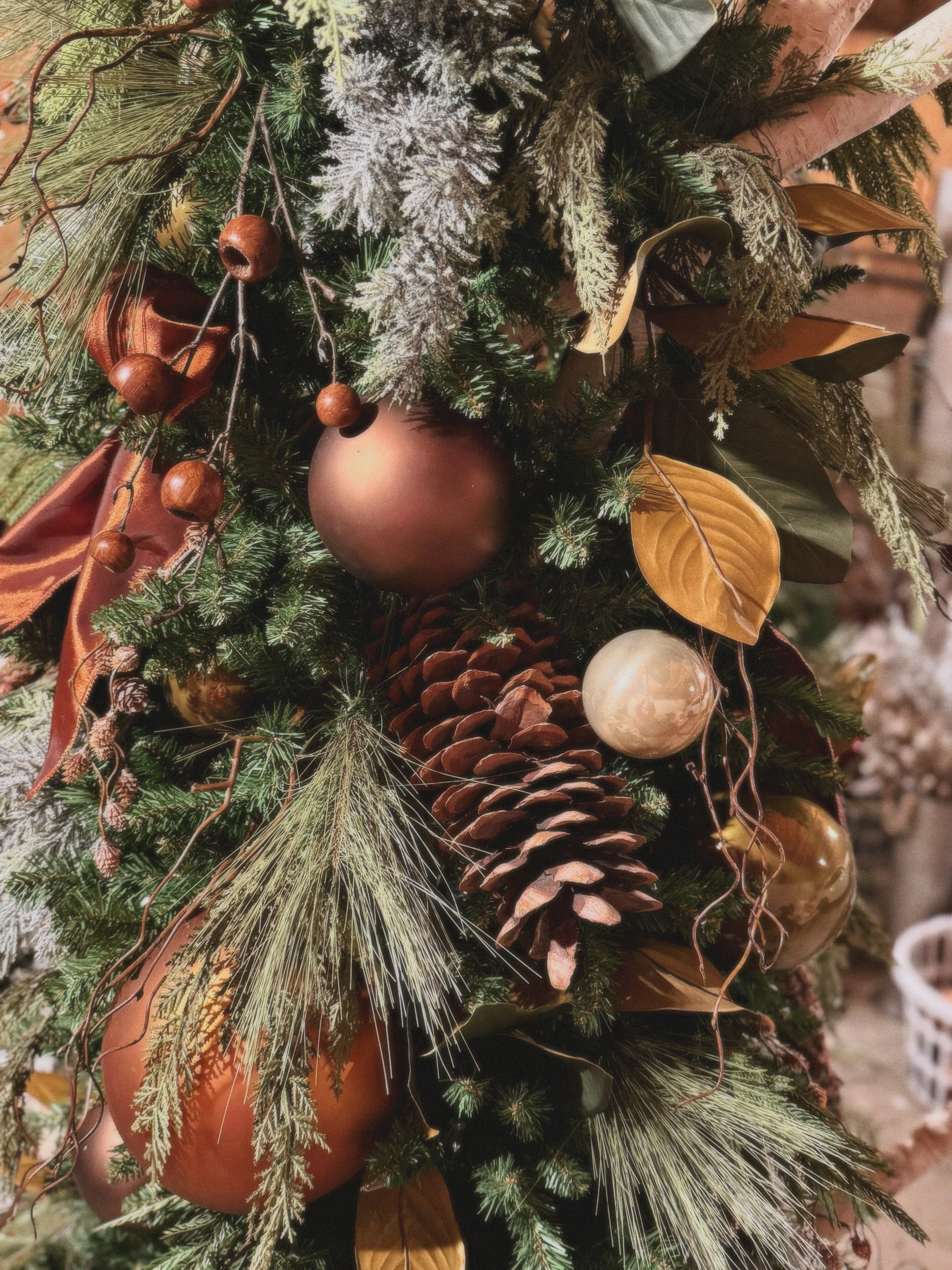 Close-up of a Christmas tree decorated with pinecones, gold and bronze ornaments, dried leaves, and greenery.