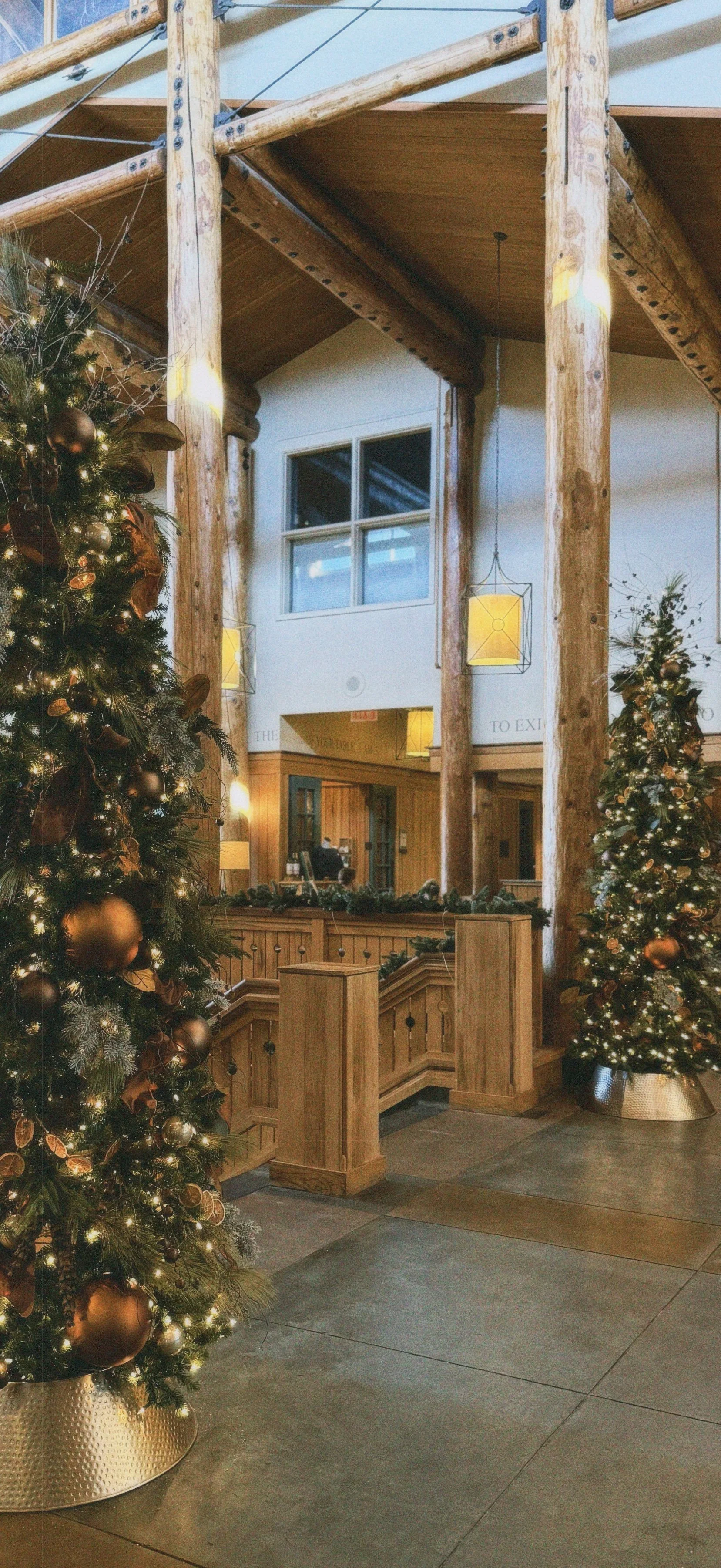 Interior of a lobby decorated for Christmas with two Christmas trees, wooden railings, and festive lighting.