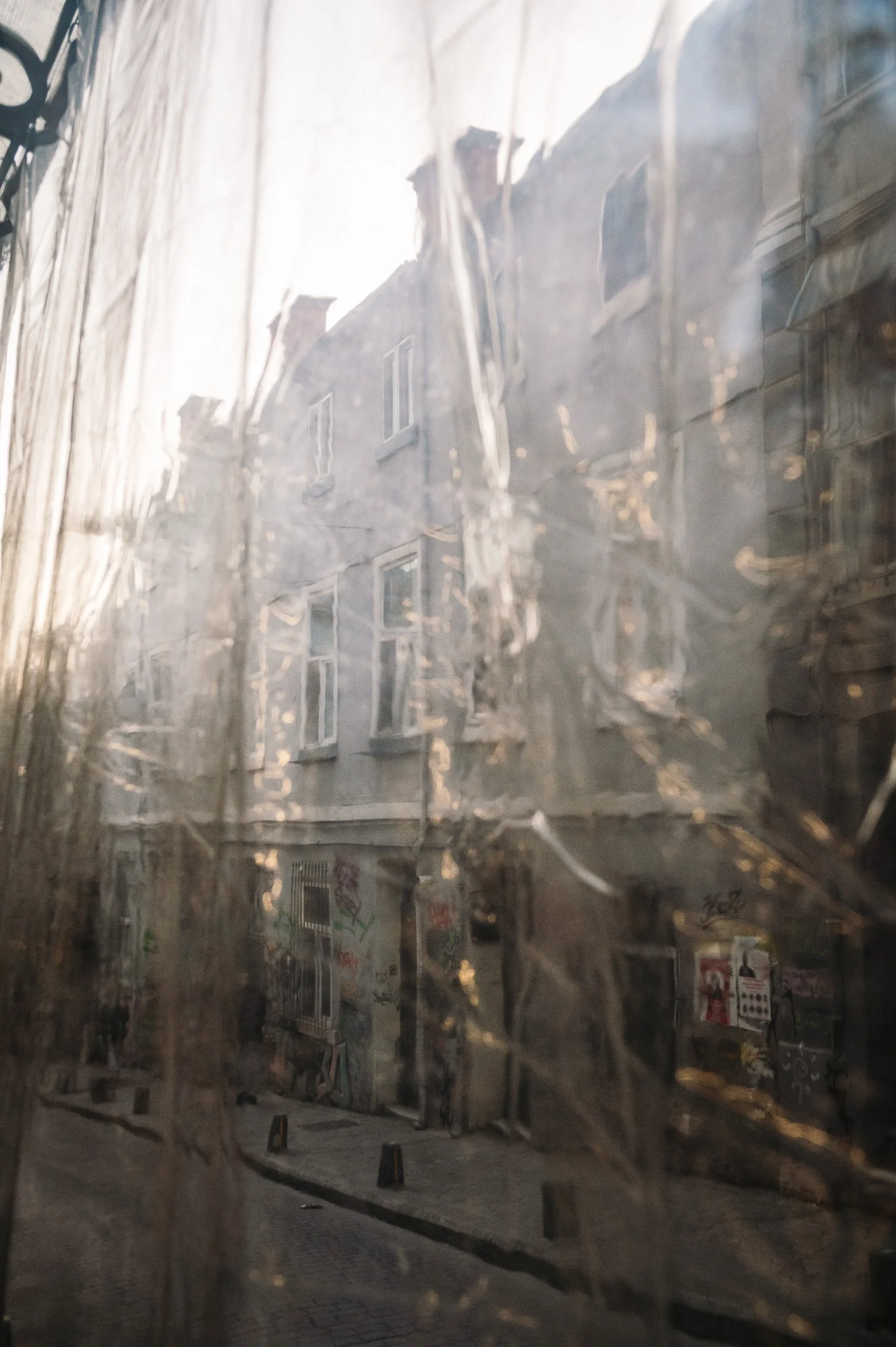 Buildings and graffiti seen through a dirty, streaked window on a city street in daylight.