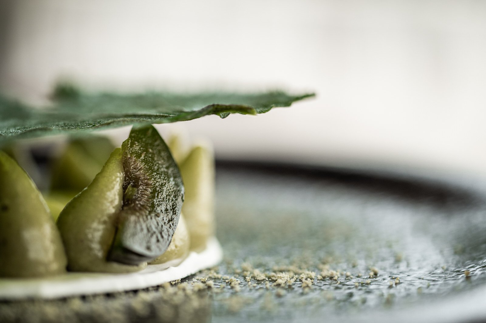 Close-up of a pile of green cardamom pods on a surface, with a leaf partially covering them, and some ground spice scattered around. Hotels, Villas, Airbnb photography. Corfu, Greece.