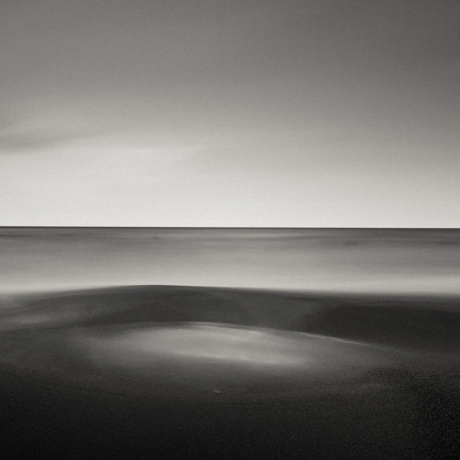 Black and white photo of a calm ocean with gentle waves and a clear horizon under a cloudless sky.