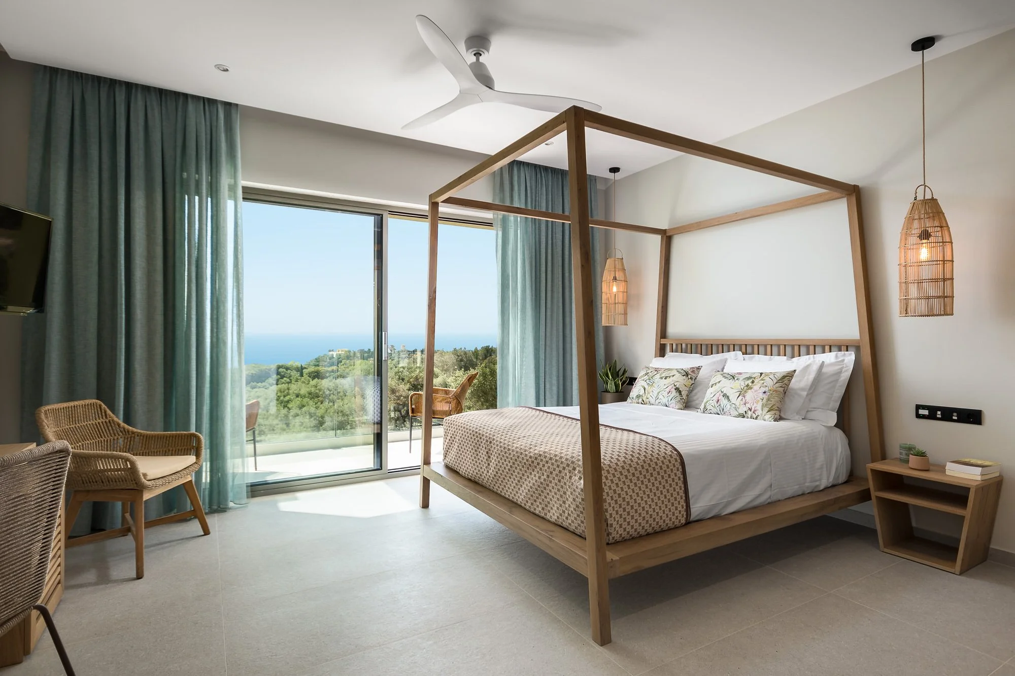 Modern bedroom with a wooden four-poster bed, hanging wicker lamps, a nightstand with books and a plant, overlooking a scenic view of trees and the ocean through sliding glass doors with blue curtains. Hotels, Villas, Airbnb photography. Corfu, Greec