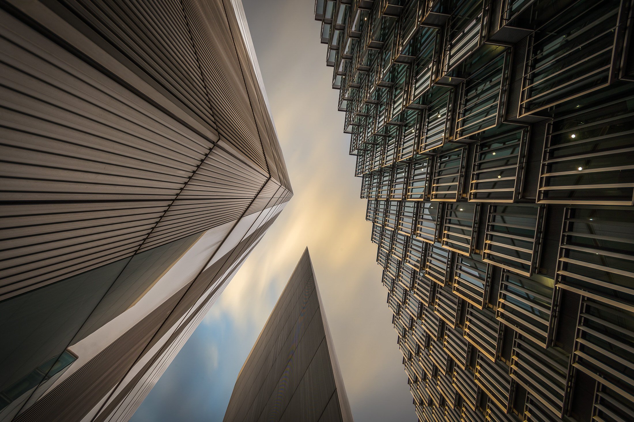 Looking up at tall modern skyscrapers with glass and metal facades against a cloudy sky. Hotels, Villas, Airbnb photography. Corfu, Greece.