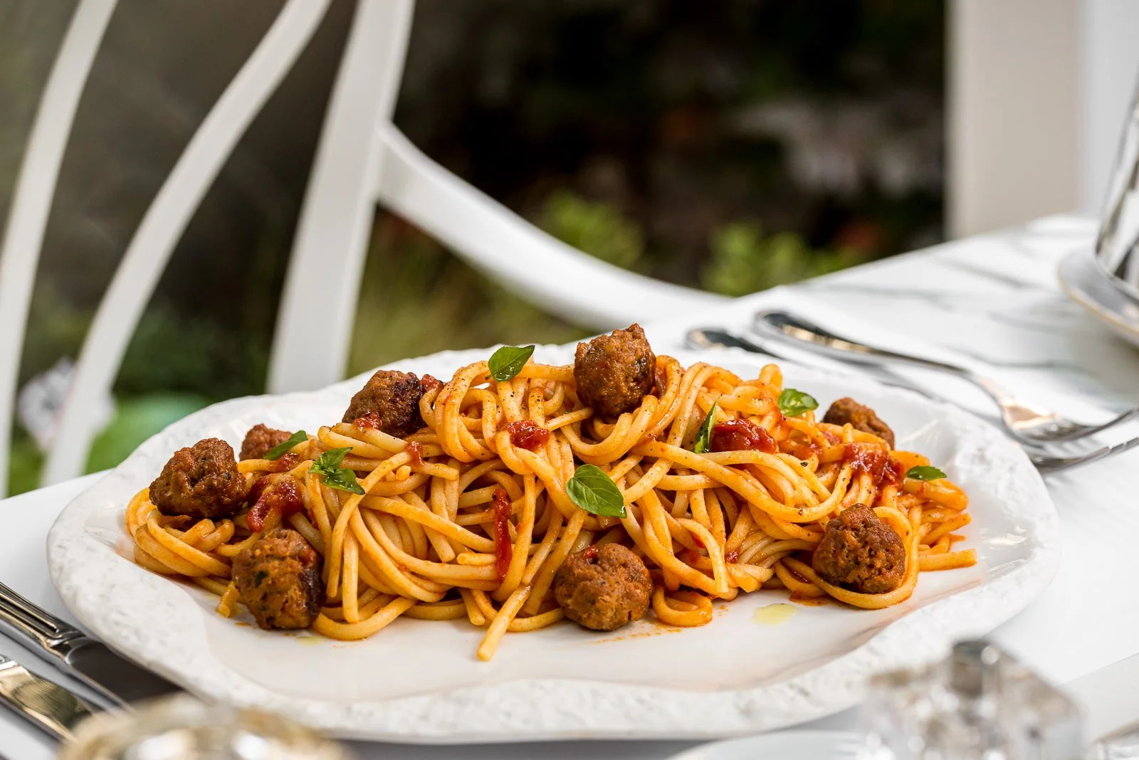 Plate of spaghetti with meatballs and tomato sauce garnished with basil, placed on a table setting. Hotels, Villas, Airbnb photography. Corfu, Greece.
