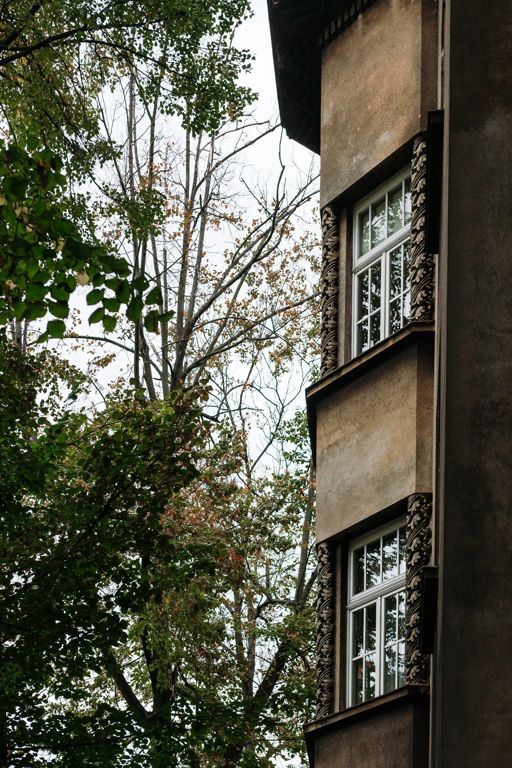 Close-up of a multi-story building with decorative window trim, with trees and overcast sky in the background.