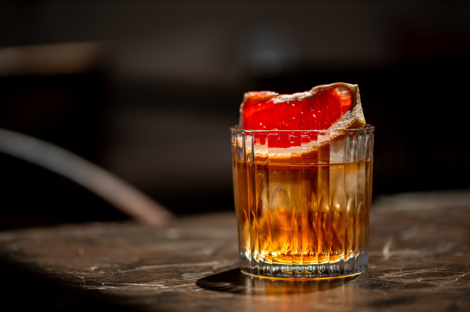 A glass of amber-colored cocktail with a grapefruit wedge garnish on a dark wooden surface.Hotels, Villas, Airbnb photography. Corfu, Greece.