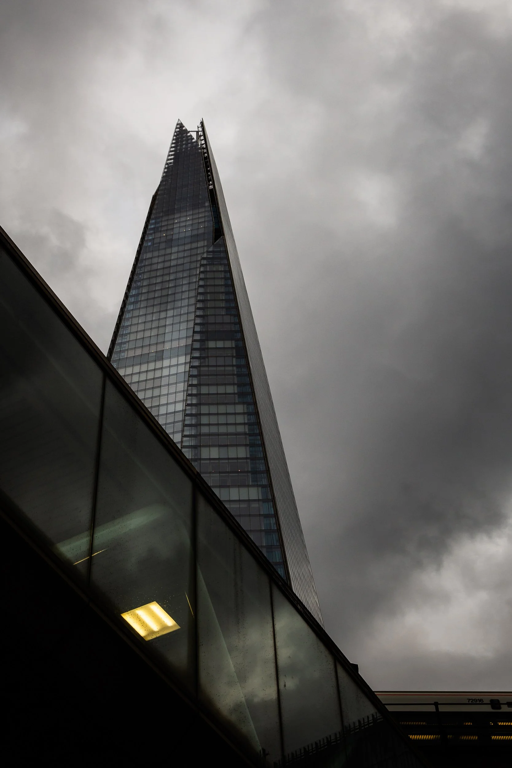 A tall, glass skyscraper with a pointed top, set against a cloudy, overcast sky.