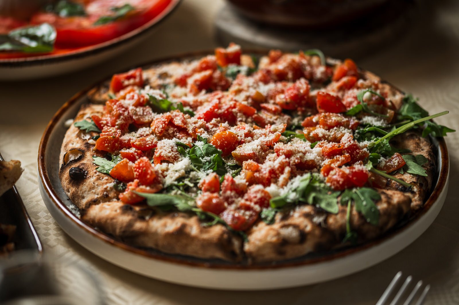 Close-up of a freshly baked pizza topped with cherry tomatoes, arugula, and grated cheese on a ceramic plate. Hotels, Villas, Airbnb photography. Corfu, Greece.
