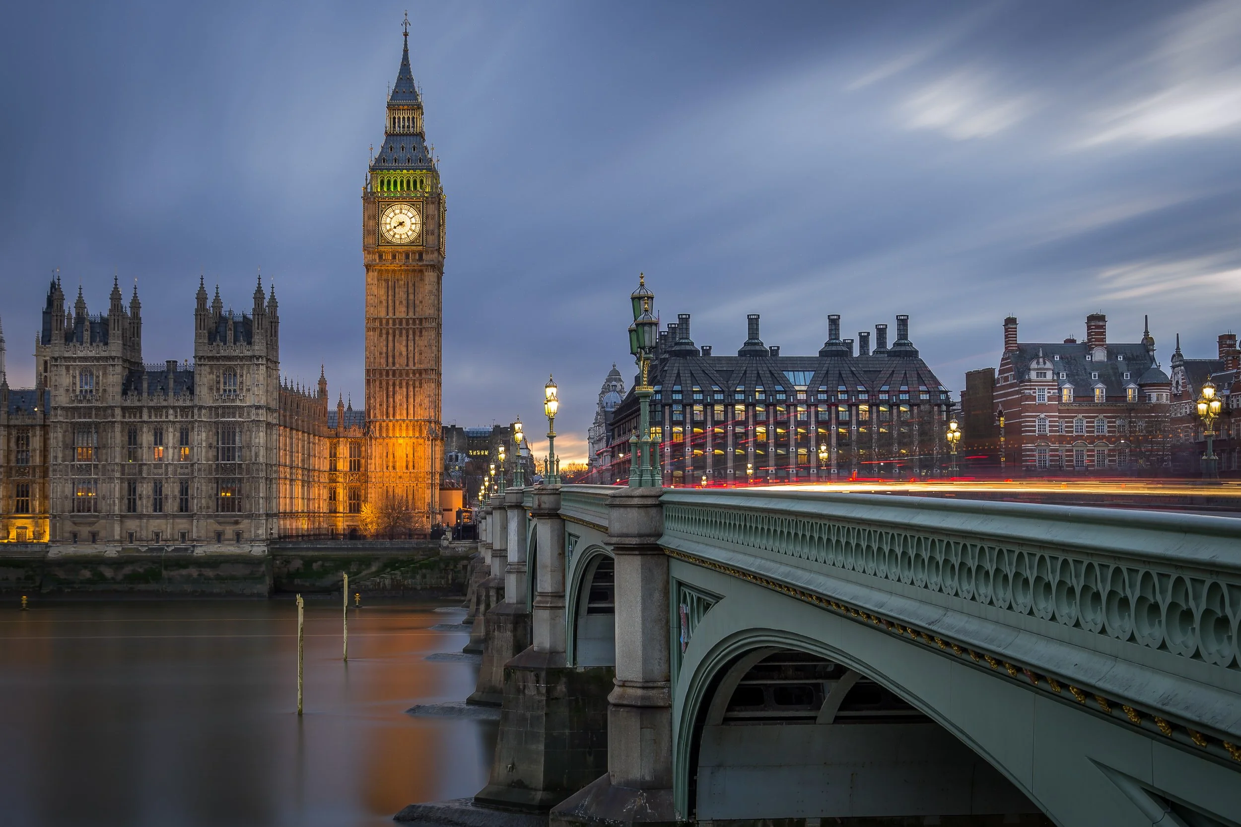 London Big Ben clock tower and Westminster Bridge at dusk with moving traffic.