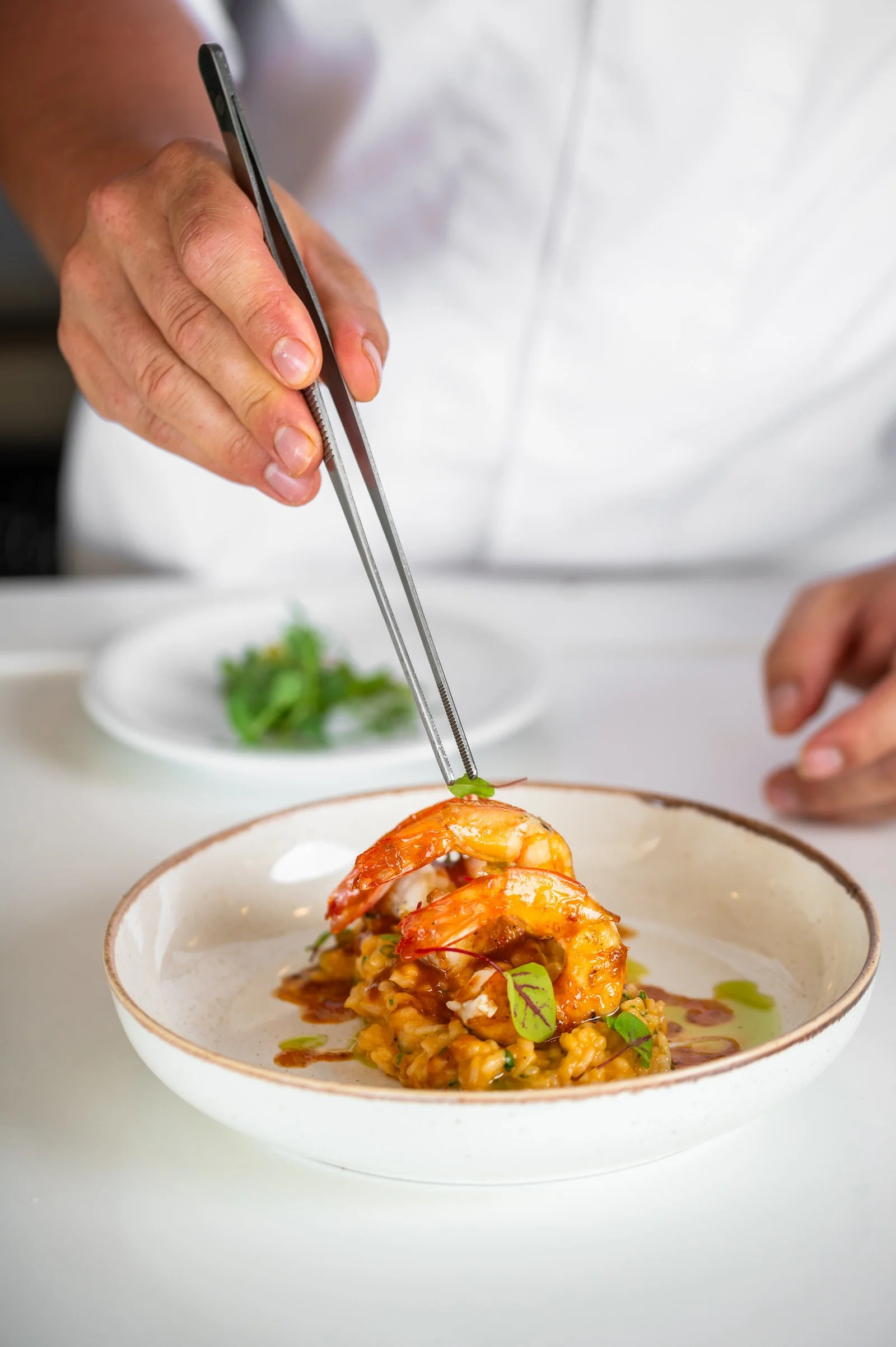 Chef garnishing a seafood dish with green herbs using tongs.Hotels, Villas, Airbnb photography. Corfu, Greece.