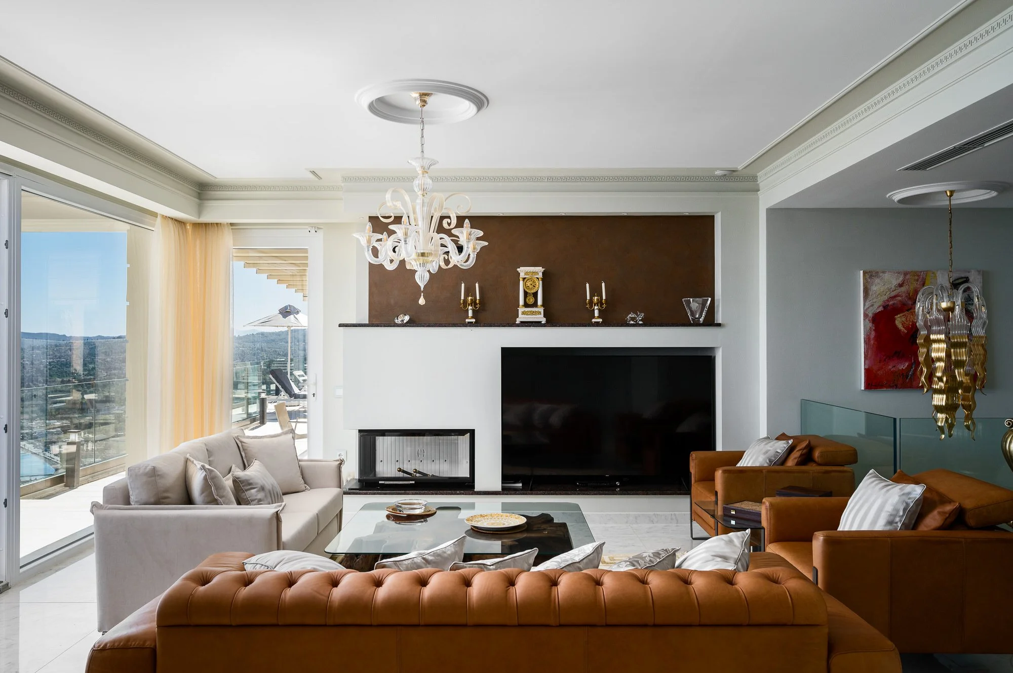 Living room with white and brown sofas, glass coffee table, fireplace, flatscreen TV, chandelier, and artwork on the wall. Hotels, Villas, Airbnb photography. Corfu, Greece.