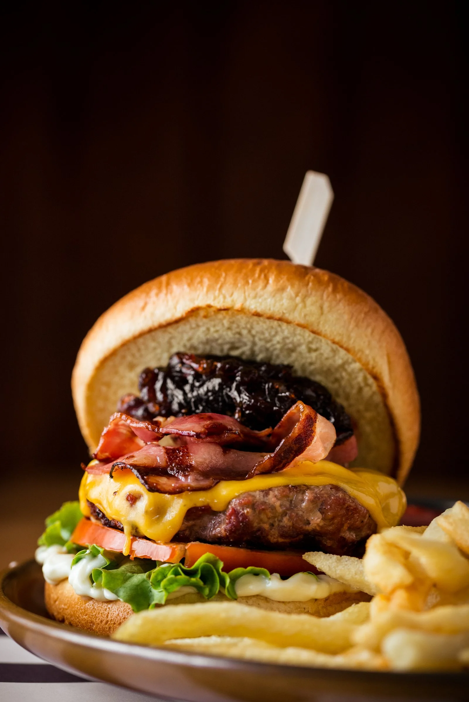 Close-up of a cheeseburger with bacon, tomato, lettuce, and fries on the side, served on a plate. Hotels, Villas, Airbnb photography. Corfu, Greece.