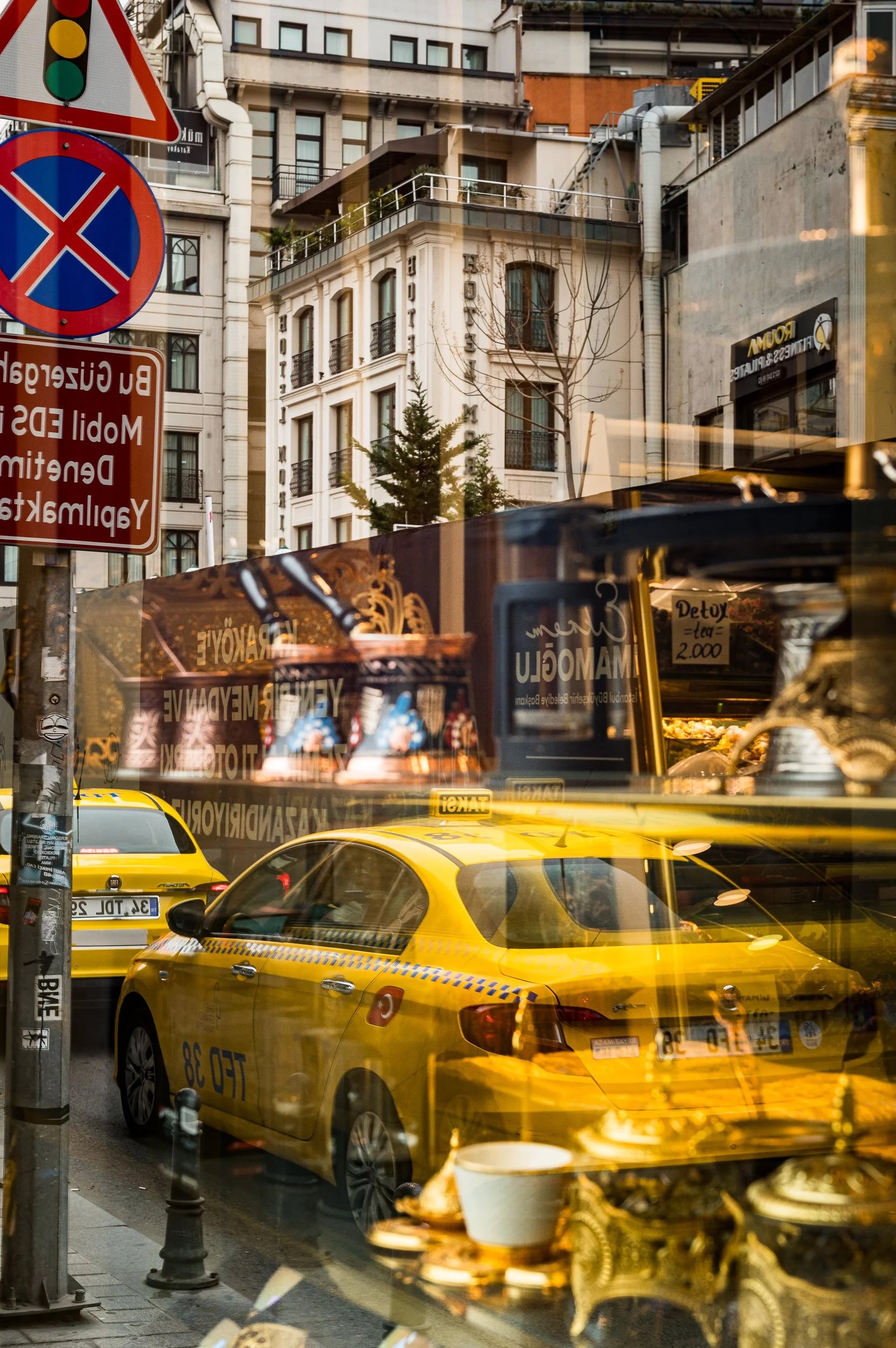Street scene with yellow taxis and buildings reflected on a glass window, with traffic signs and a cafe display.