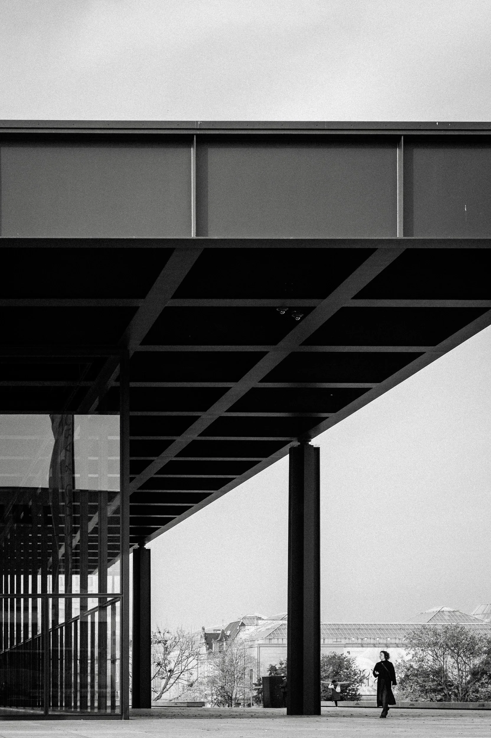 Black and white photo of a modern building with overhanging roof and large support columns, with a person walking outside.  Hotels, Villas, Airbnb photography. Corfu, Greece.