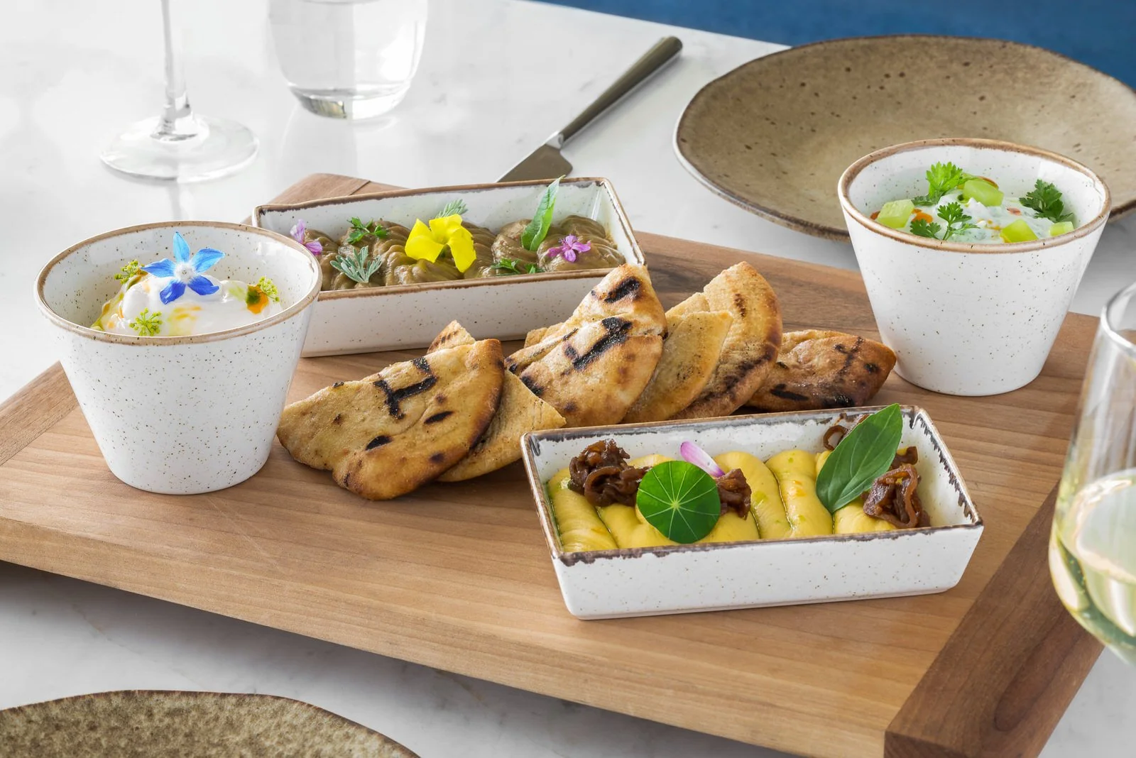 Assorted dishes including naan bread, small bowls of curry with garnishes, and a side of yellow pickled vegetables with herbs on a wooden platter. Hotels, Villas, Airbnb photography. Corfu, Greece.