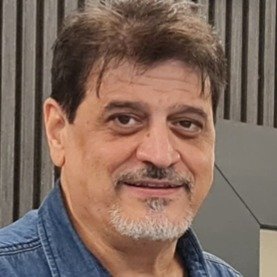 Portret van een man met bruin haar, een lichte baard en een donkere achtergrond.