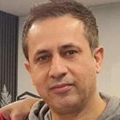 Portret van een man met kort, donker haar, op een lichte achtergrond met kantoorruimte.