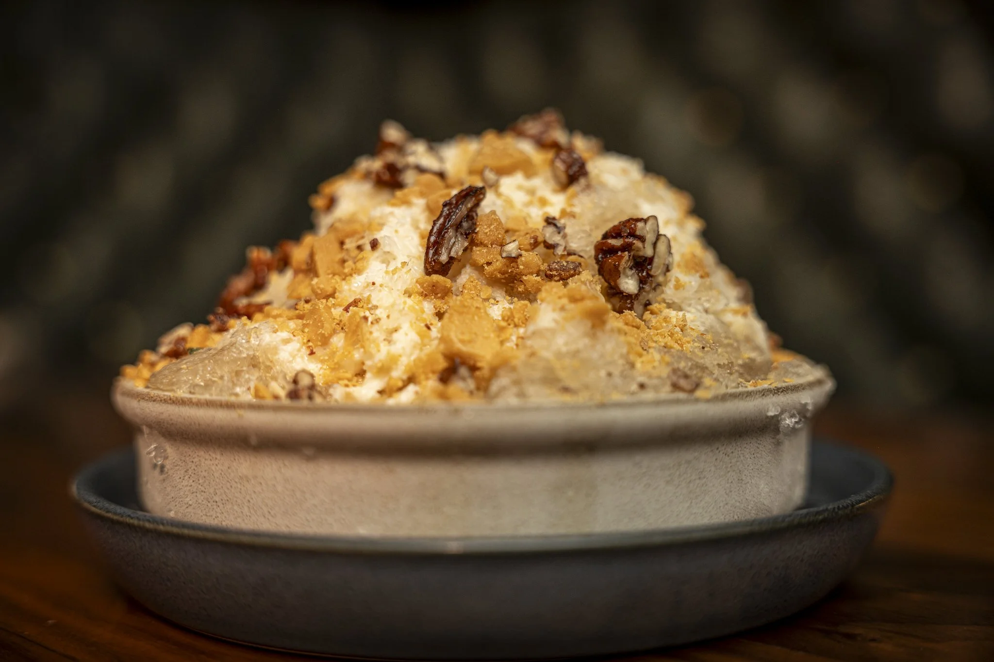 Close-up of a bowl of mashed potatoes topped with chopped pecans and bread crumbs