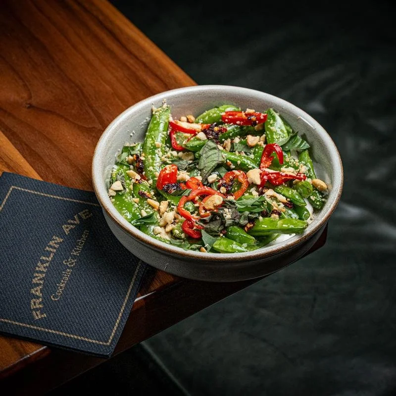 Fresh green salad with red and green chili slices, chopped nuts, and basil leaves in a bowl.