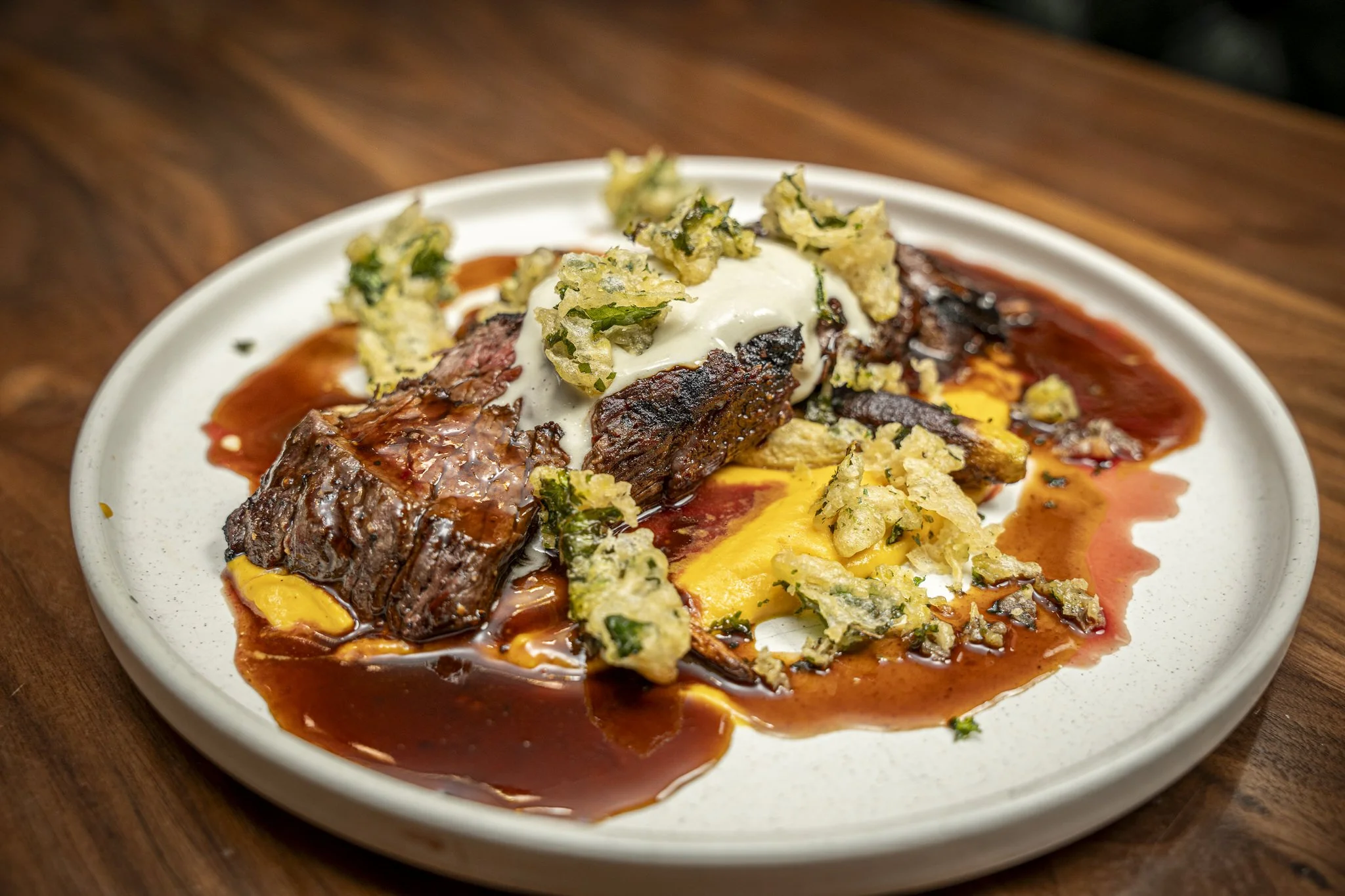 Hearty plate of braised beef short ribs with mashed potatoes, topped with sour cream and crispy fried herbs, on a white dish