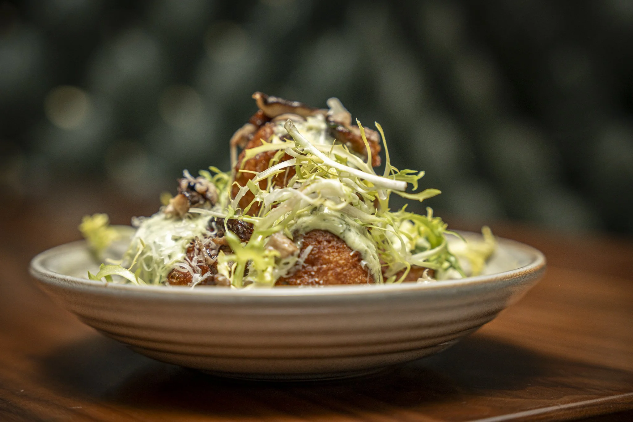 Dish with fried breaded item topped with shredded lettuce, cabbage, creamy dressing, and dark sauce on a decorative plate.