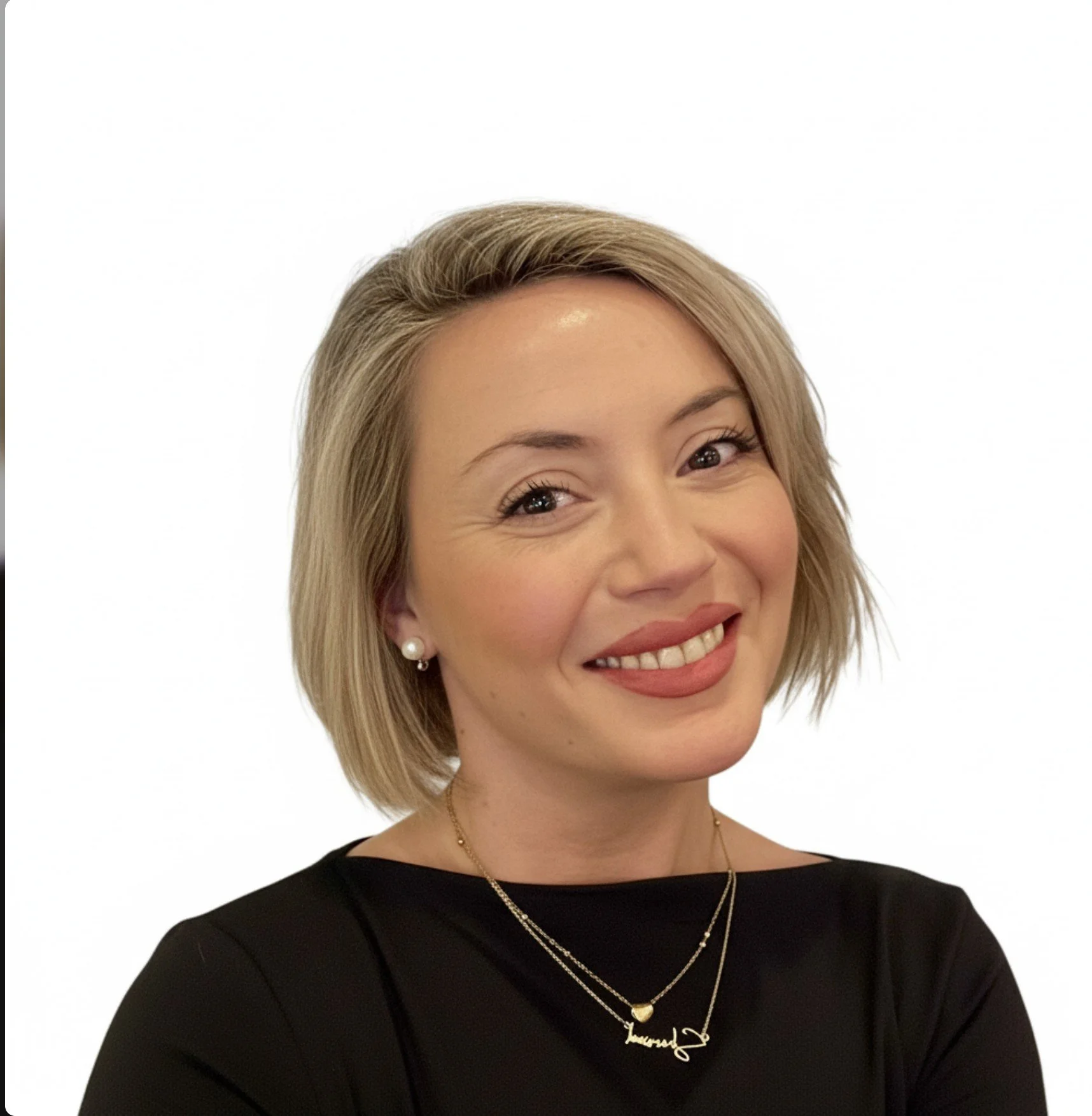 Portrait of a woman with short blonde hair smiling, wearing a black top, pearl earrings, and layered necklaces against a plain white background.