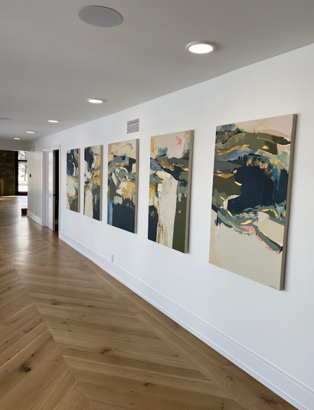 A hallway with white walls and wooden flooring displays six abstract landscape paintings.